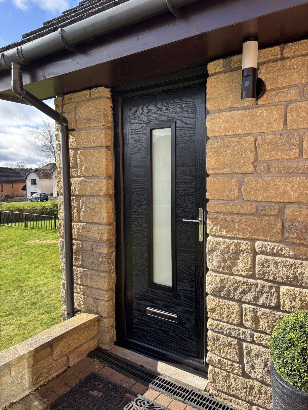 A black composite front door set in a sandstone surround