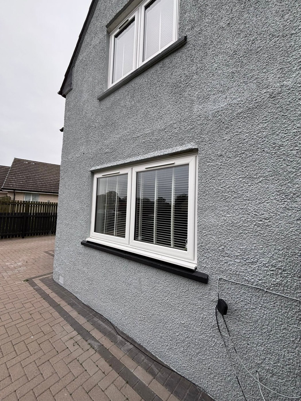 A smooth grey-coated render wall with modern uPVC windows